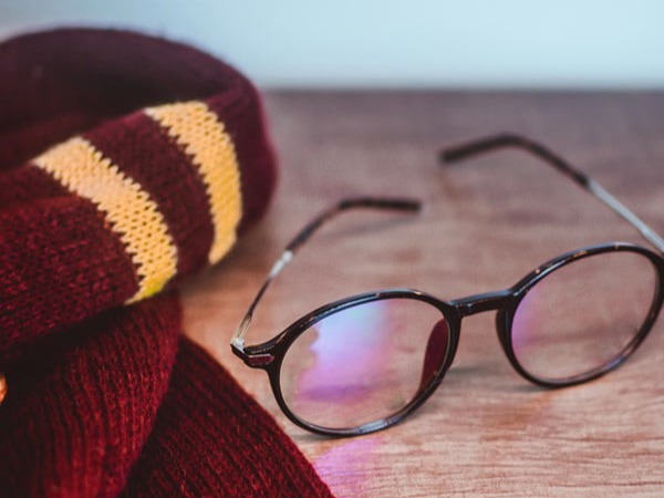 A pair of round-framed glasses with reflective lenses and a red and yellow striped scarf are placed on a wooden surface.